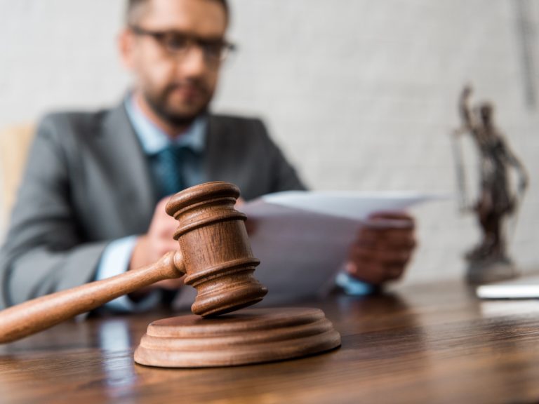 close-up view of wooden hammer and judge working with papers behind